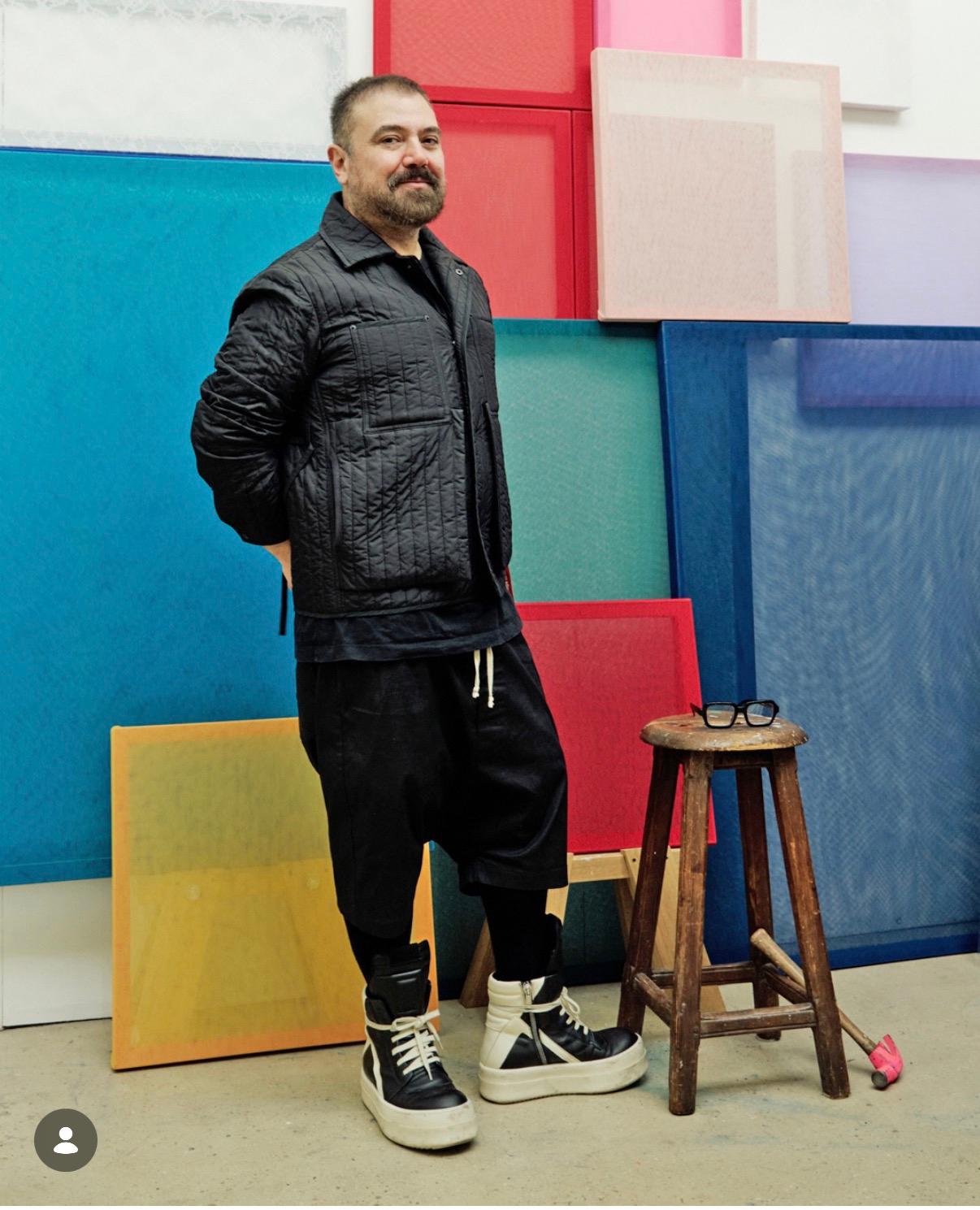 Emilio de la Morena in his studio, standing before a wall of coloured tulle panels